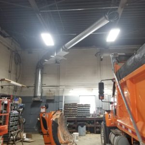 Image shows the ductwork leading from a geothermal heat exchanger into the center of the maintenance garage for the Town of Hamilton. A snowplow and other equipment can be seen.