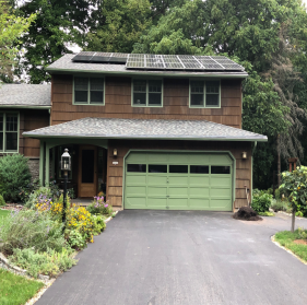 A brown split level ranch with a green garage door and solar panels on the top